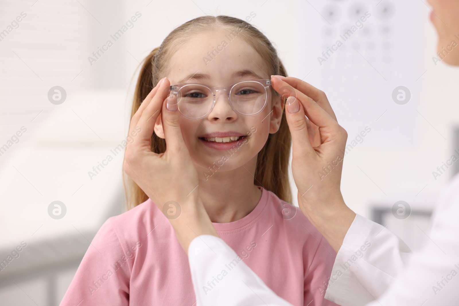 Photo of Vision testing. Ophthalmologist giving glasses to little girl in clinic, closeup