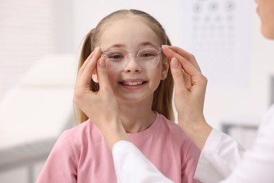 Photo of Vision testing. Ophthalmologist giving glasses to little girl in clinic, closeup