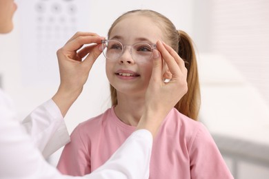 Photo of Vision testing. Ophthalmologist giving glasses to little girl in clinic, closeup