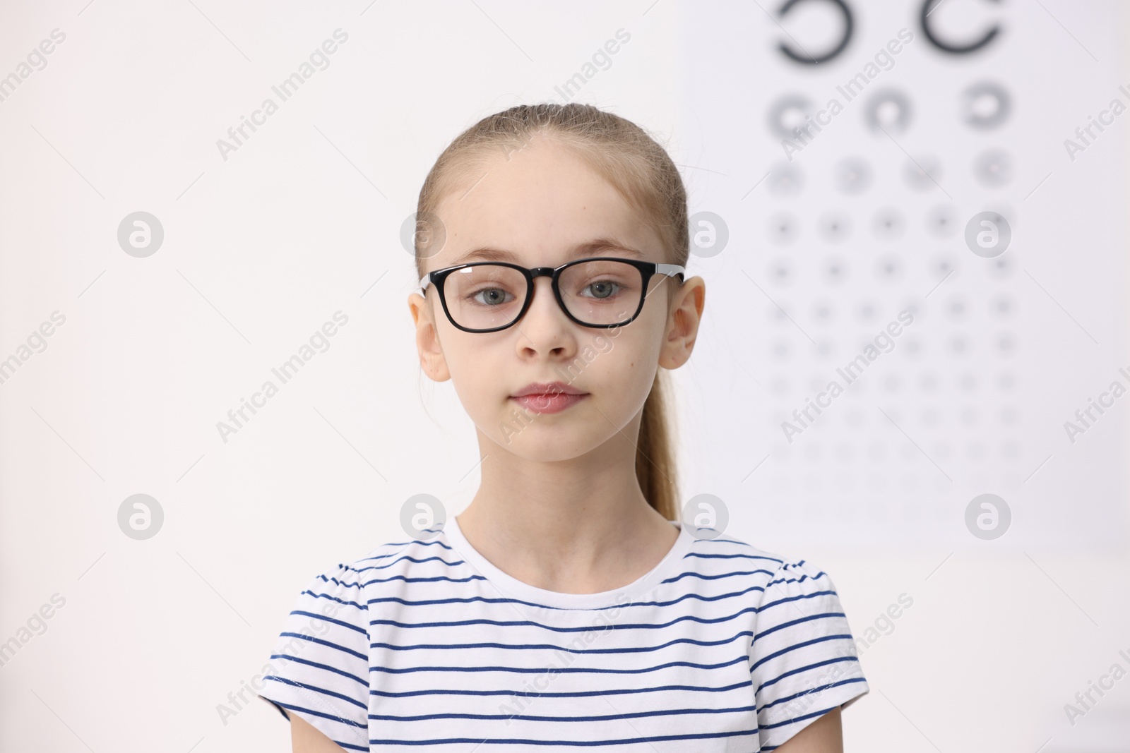 Photo of Little girl wearing glasses near vision test chart at ophthalmologist office