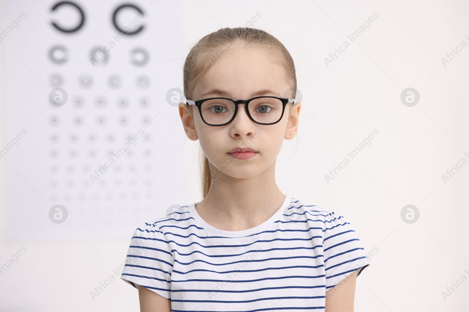 Photo of Little girl wearing glasses near vision test chart at ophthalmologist office