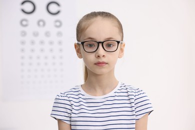 Photo of Little girl wearing glasses near vision test chart at ophthalmologist office