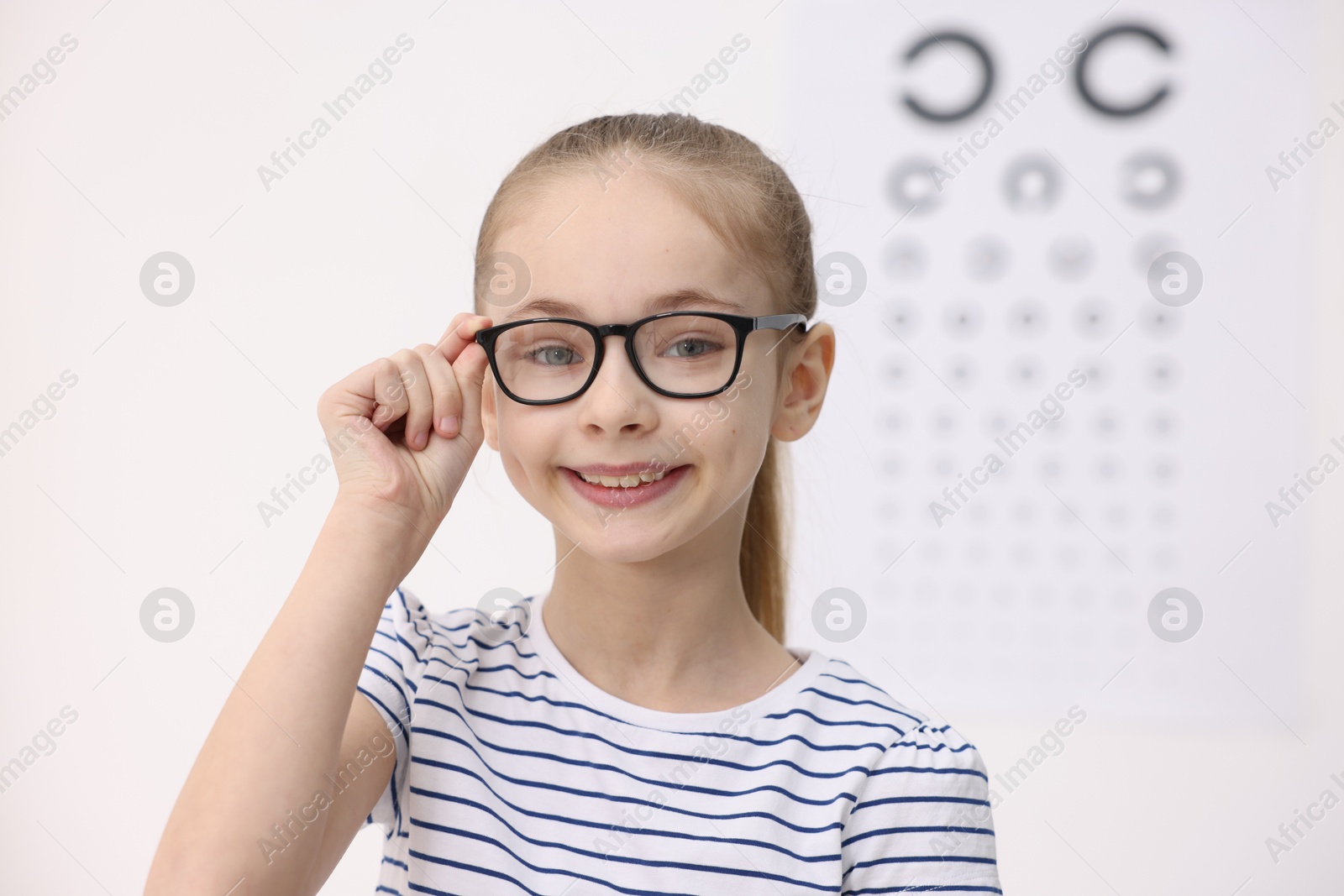 Photo of Little girl wearing glasses near vision test chart at ophthalmologist office