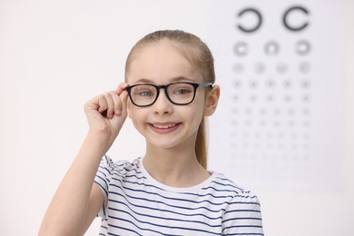 Photo of Little girl wearing glasses near vision test chart at ophthalmologist office