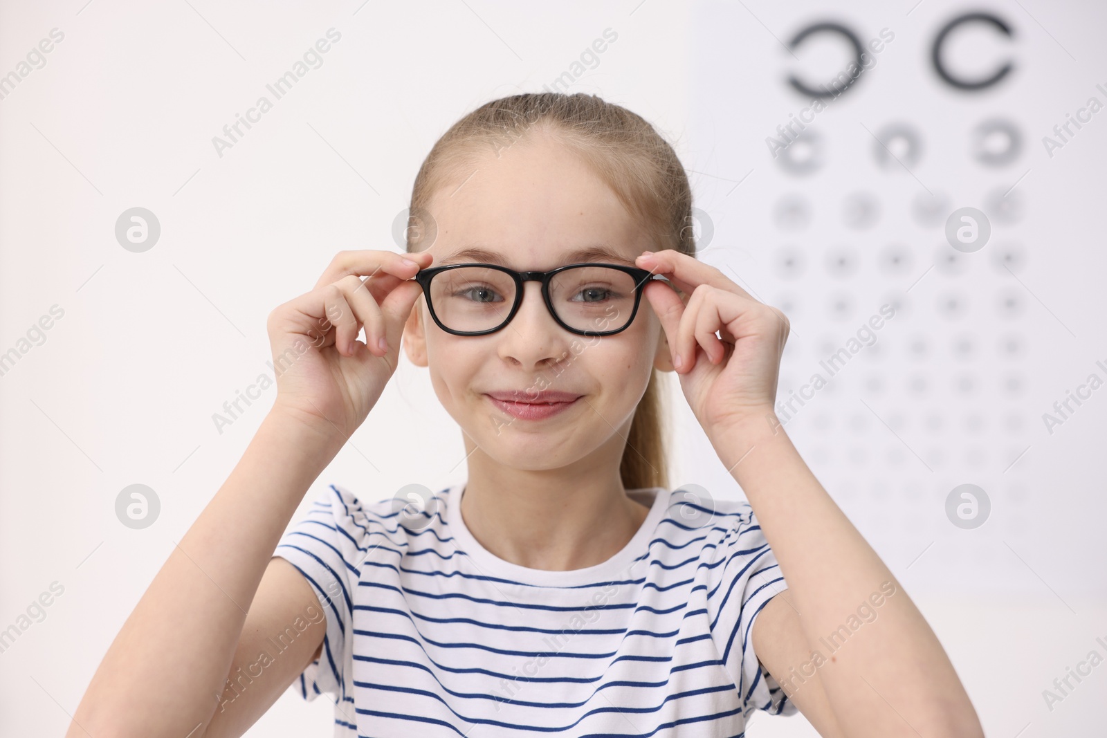 Photo of Little girl wearing glasses near vision test chart at ophthalmologist office