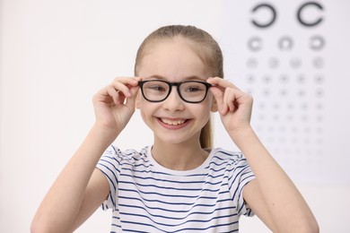 Photo of Little girl wearing glasses near vision test chart at ophthalmologist office