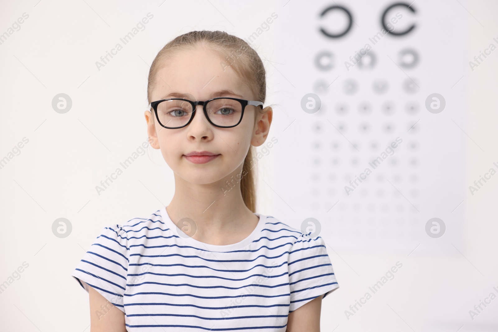 Photo of Little girl wearing glasses near vision test chart at ophthalmologist office, space for text