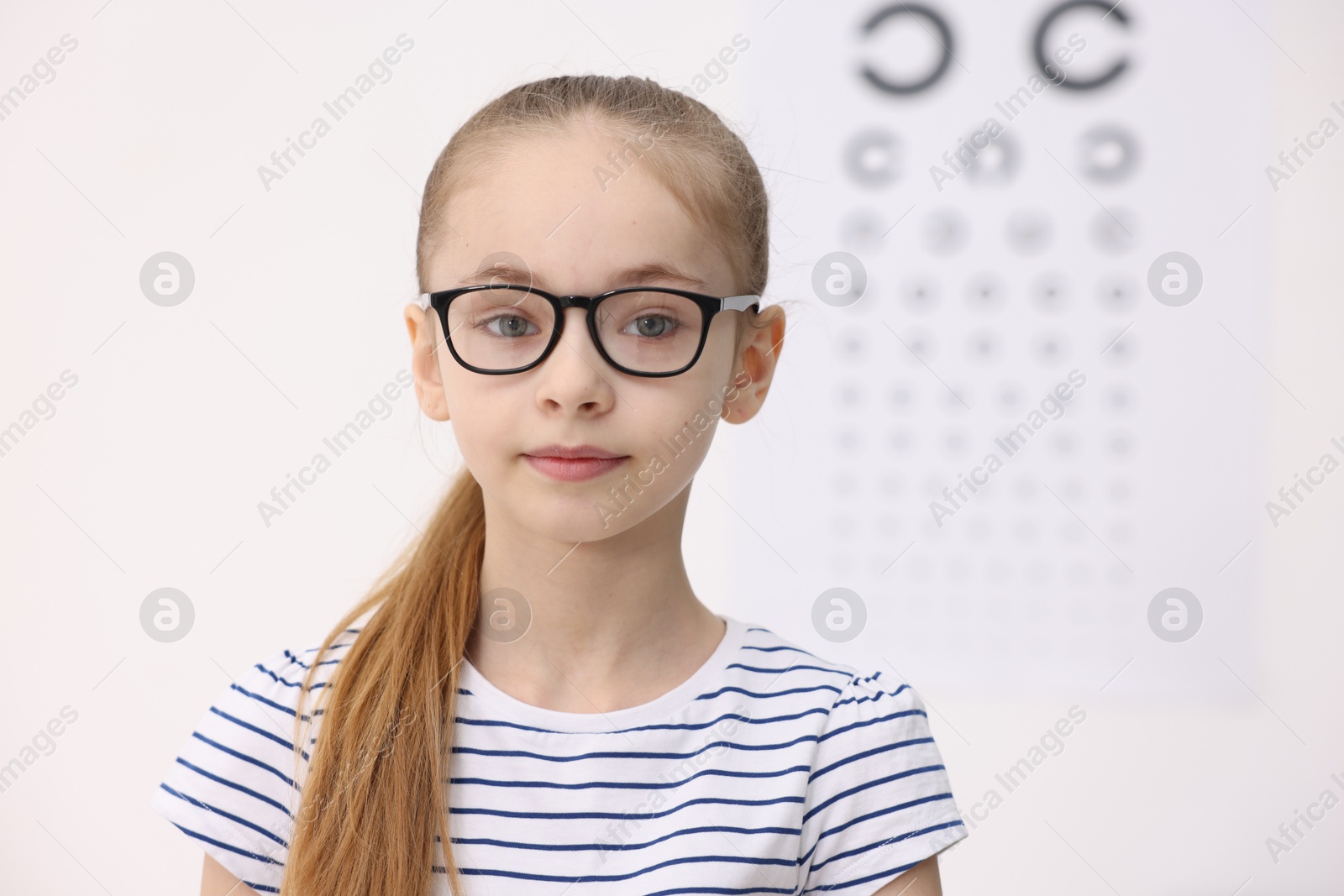 Photo of Little girl wearing glasses near vision test chart at ophthalmologist office, space for text