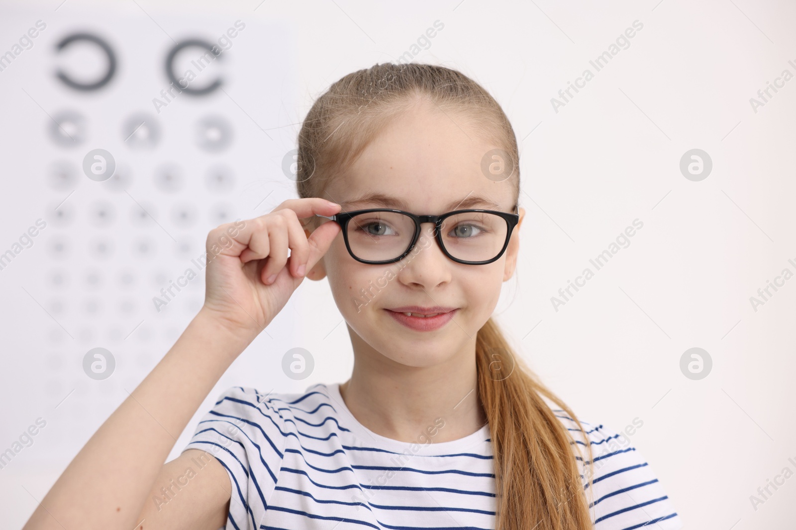 Photo of Little girl wearing glasses near vision test chart at ophthalmologist office