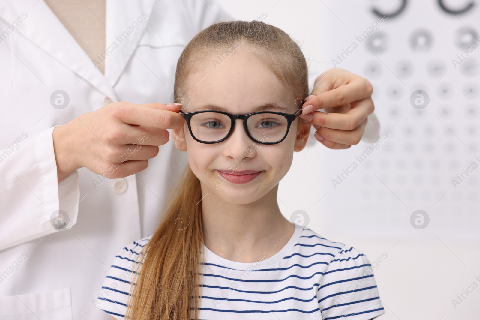 Photo of Vision testing. Ophthalmologist giving glasses to little girl in clinic, closeup