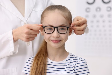 Photo of Vision testing. Ophthalmologist giving glasses to little girl in clinic, closeup