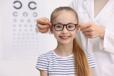 Photo of Vision testing. Ophthalmologist giving glasses to little girl in clinic, closeup