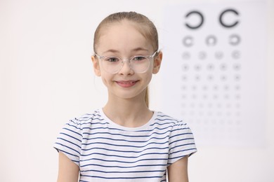 Photo of Little girl wearing glasses near vision test chart at ophthalmologist office, space for text