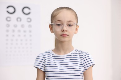 Photo of Little girl wearing glasses near vision test chart at ophthalmologist office