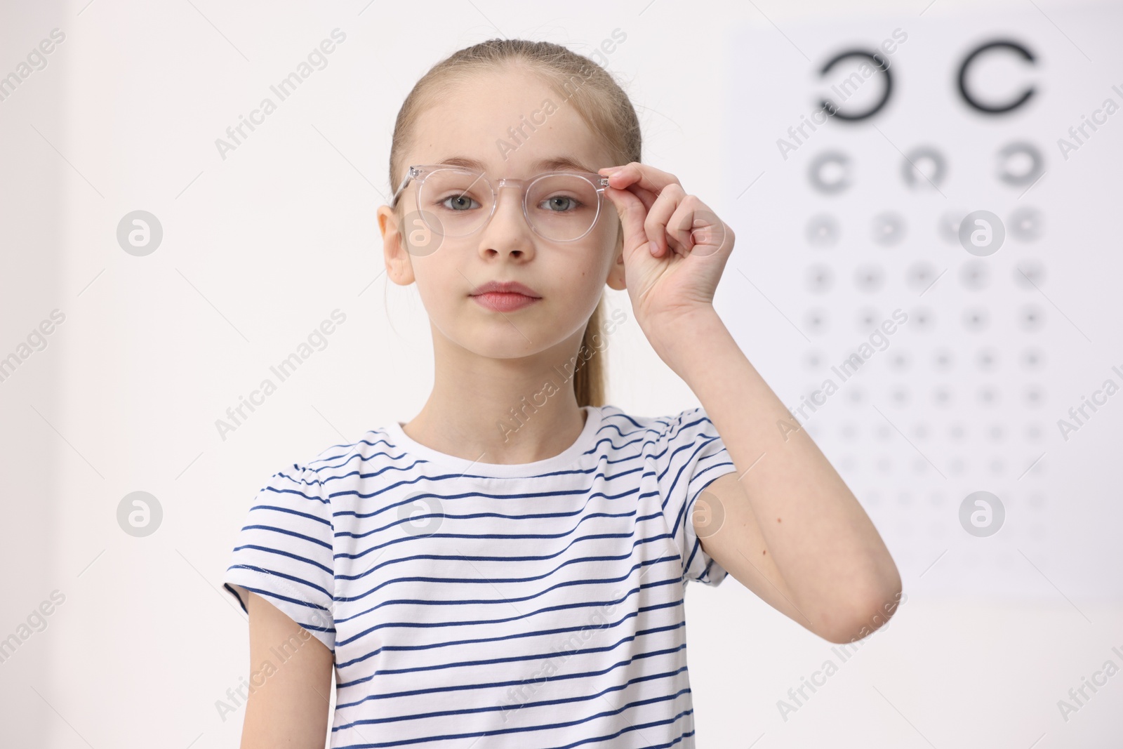 Photo of Little girl wearing glasses near vision test chart at ophthalmologist office