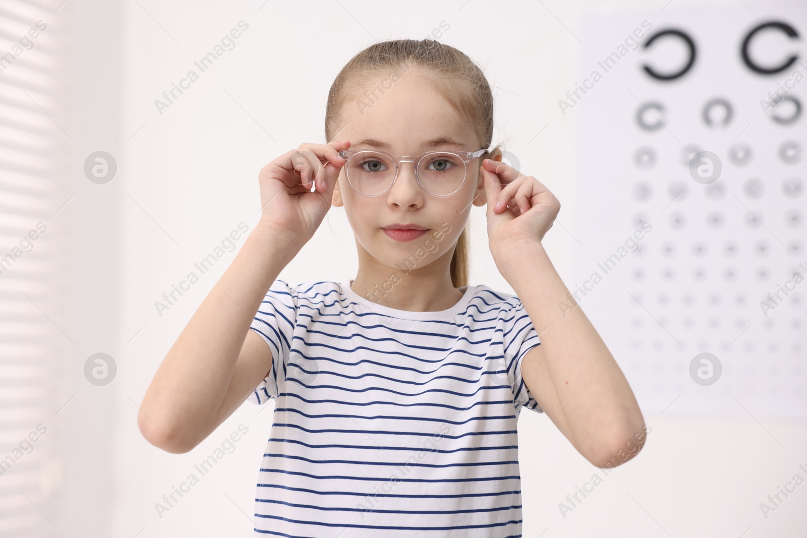 Photo of Little girl wearing glasses near vision test chart at ophthalmologist office