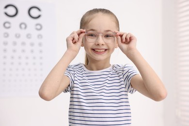 Photo of Little girl wearing glasses near vision test chart at ophthalmologist office