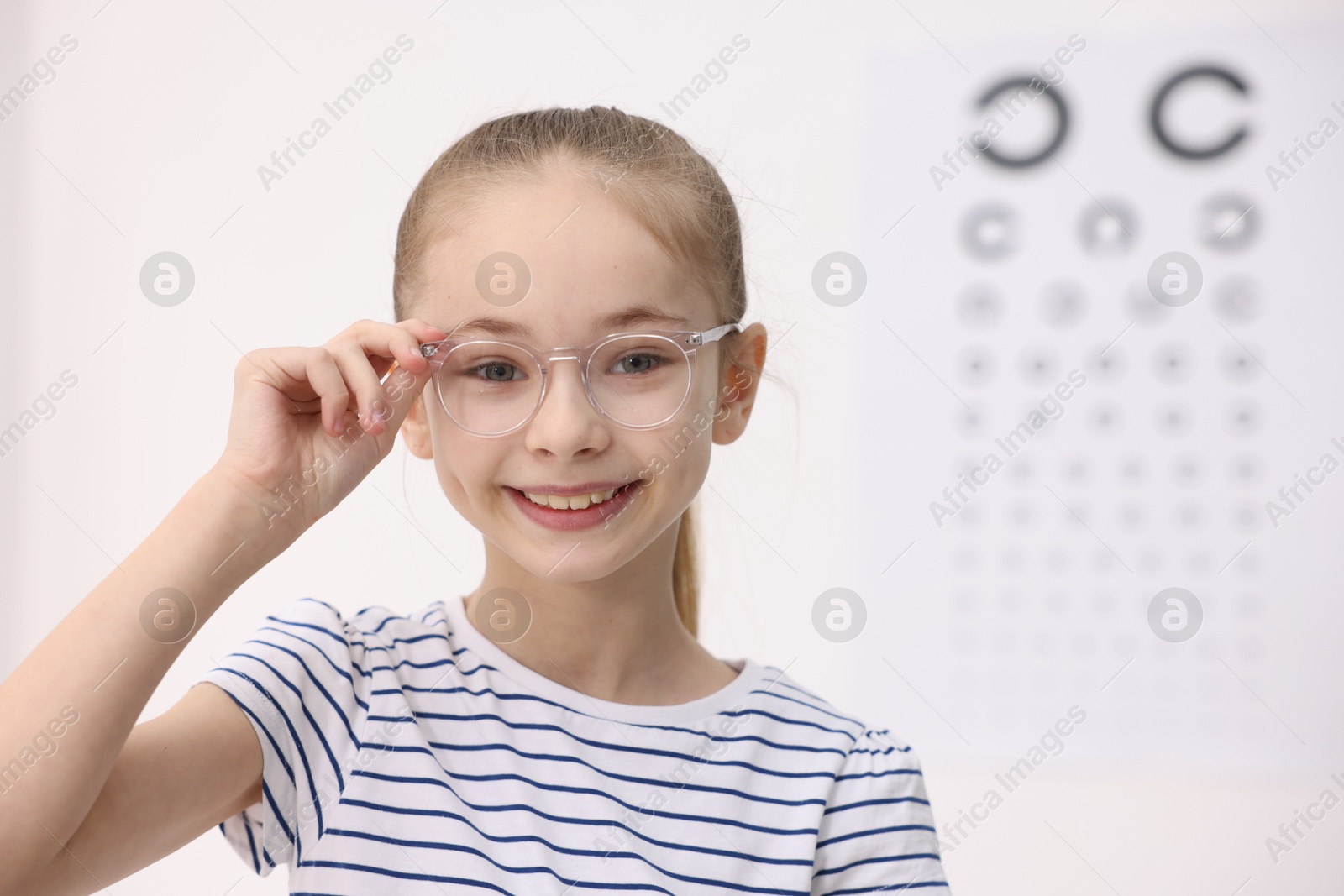 Photo of Little girl wearing glasses near vision test chart at ophthalmologist office, space for text