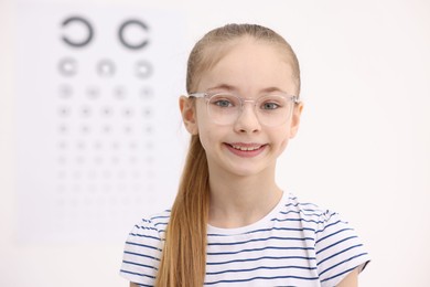 Photo of Little girl wearing glasses near vision test chart at ophthalmologist office, space for text