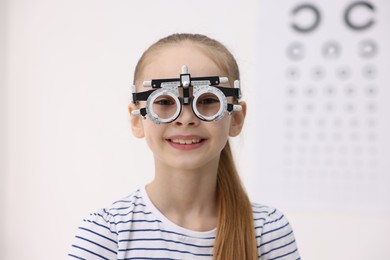 Photo of Little girl with trial frame near vision test chart at ophthalmologist office