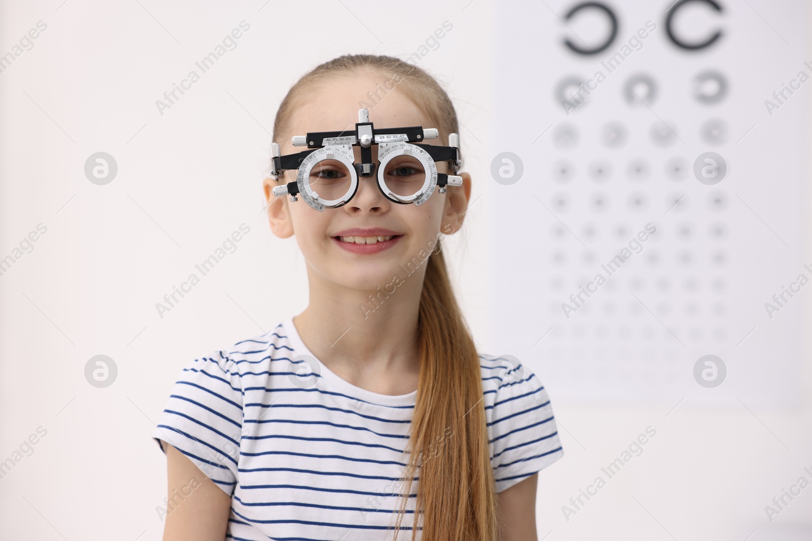 Photo of Little girl with trial frame near vision test chart at ophthalmologist office