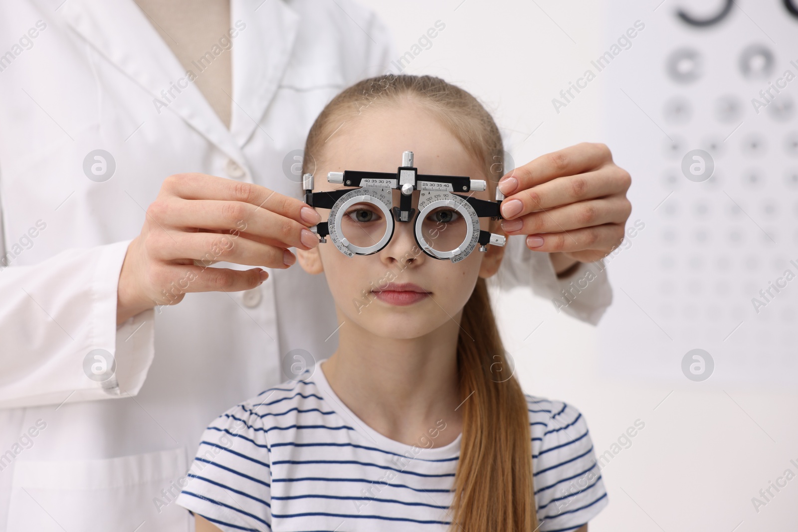 Photo of Ophthalmologist examining girl's vision with trial frame in clinic, closeup