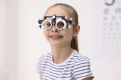 Photo of Little girl with trial frame near vision test chart at ophthalmologist office