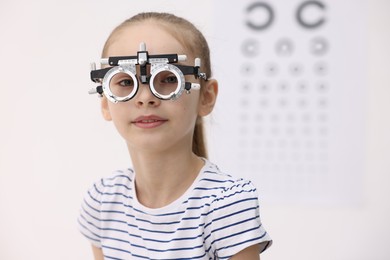 Photo of Little girl with trial frame near vision test chart at ophthalmologist office, space for text