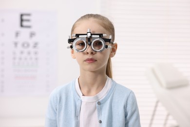 Photo of Little girl with trial frame near vision test chart at ophthalmologist office