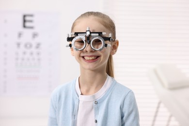 Photo of Little girl with trial frame near vision test chart at ophthalmologist office