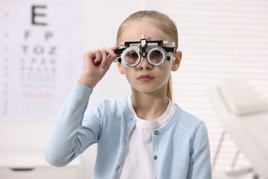 Photo of Little girl with trial frame near vision test chart at ophthalmologist office