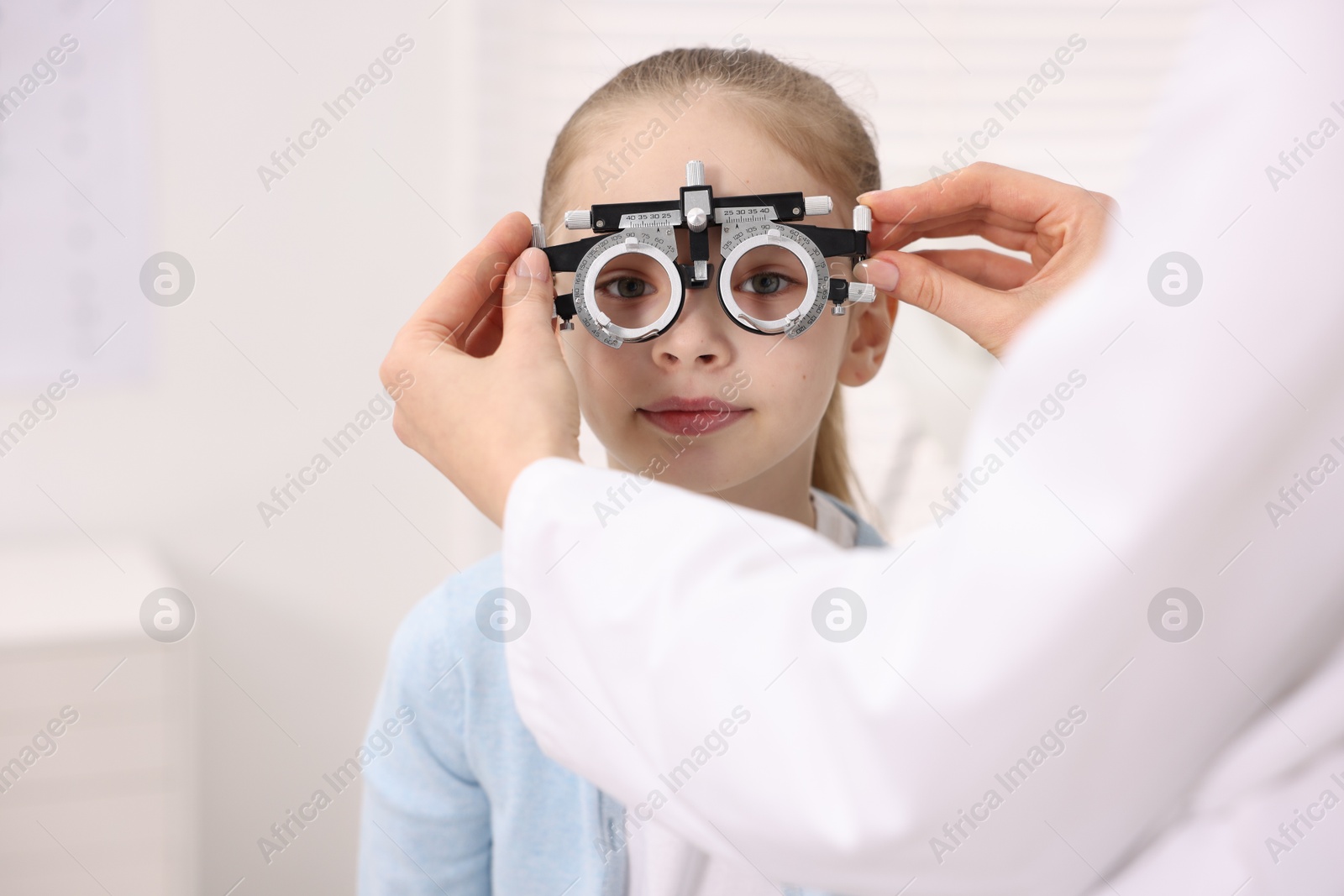 Photo of Ophthalmologist examining girl's vision with trial frame in clinic, closeup