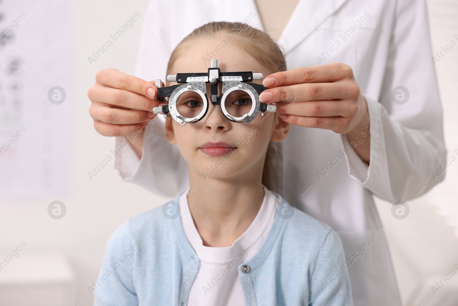 Photo of Ophthalmologist examining girl's vision with trial frame in clinic, closeup