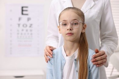 Photo of Little girl with glasses and ophthalmologist in office, space for text