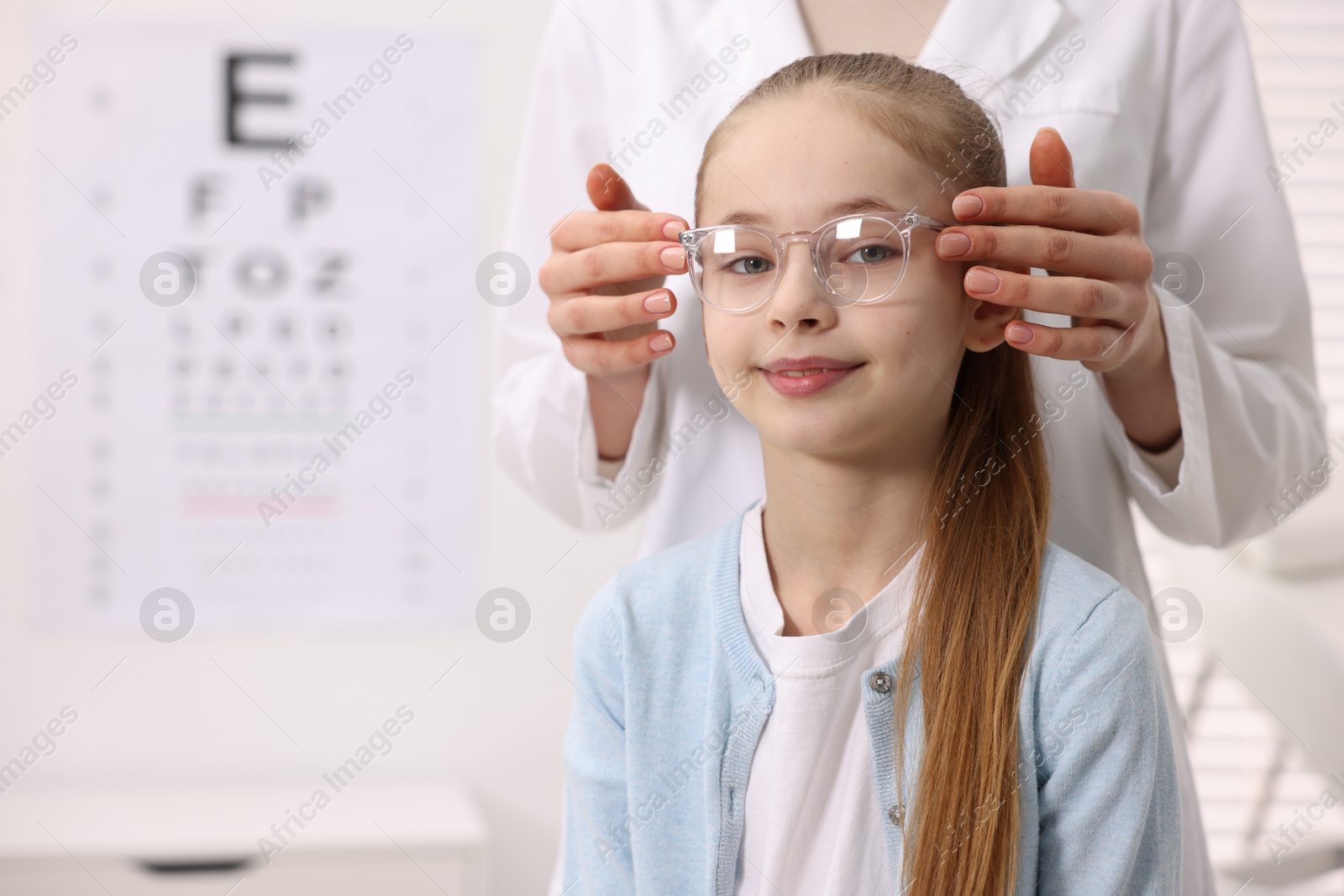 Photo of Vision testing. Ophthalmologist giving glasses to little girl in clinic, closeup