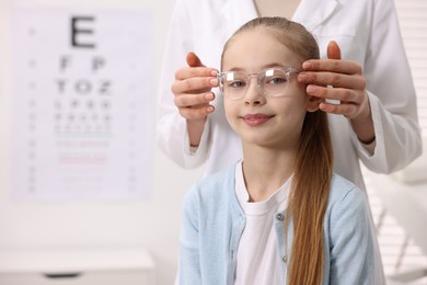 Photo of Vision testing. Ophthalmologist giving glasses to little girl in clinic, closeup