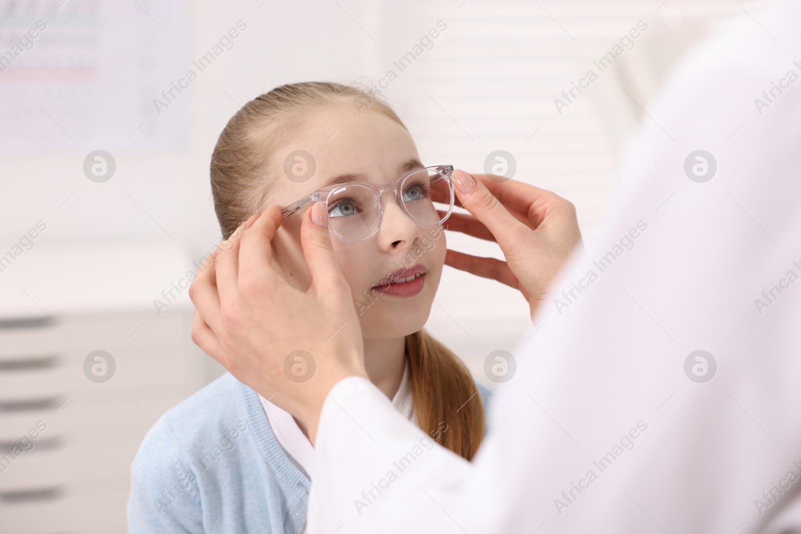 Photo of Vision testing. Ophthalmologist giving glasses to little girl in clinic, closeup