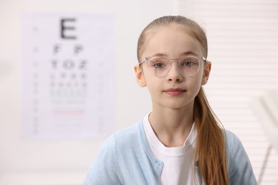 Photo of Little girl wearing glasses near vision test chart at ophthalmologist office, space for text