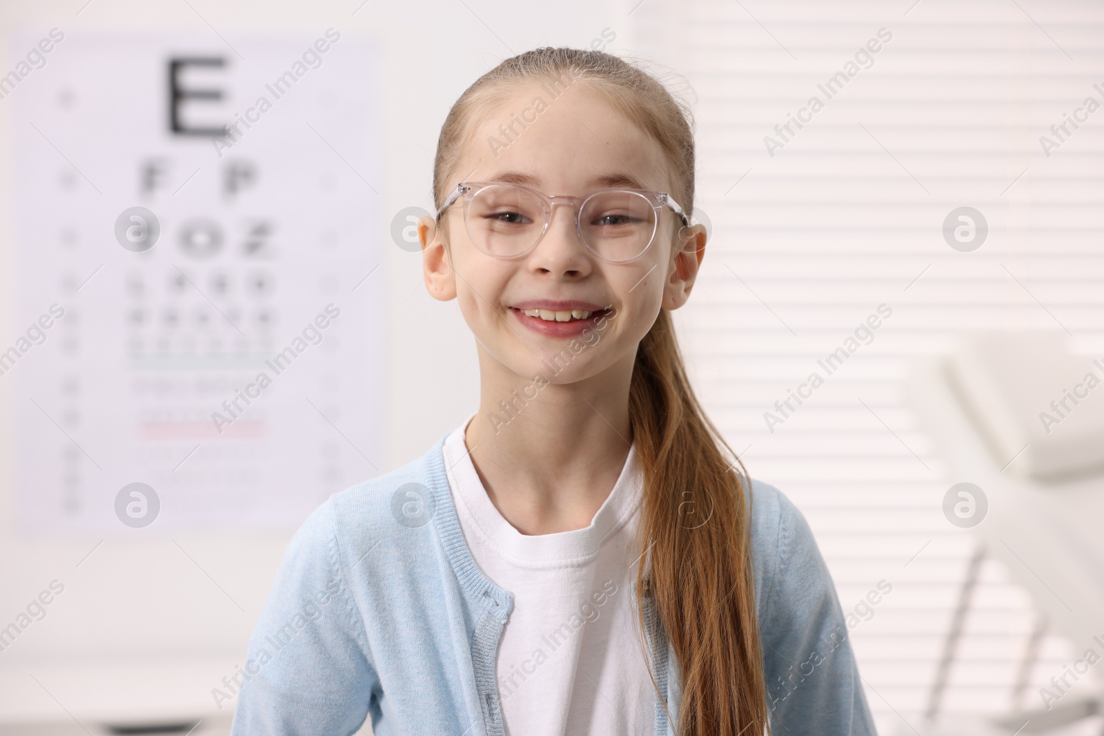 Photo of Little girl wearing glasses near vision test chart at ophthalmologist office