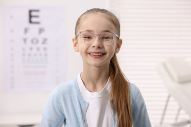 Photo of Little girl wearing glasses near vision test chart at ophthalmologist office