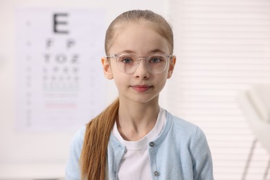 Photo of Little girl wearing glasses near vision test chart at ophthalmologist office