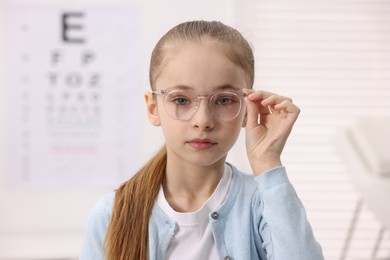 Photo of Little girl wearing glasses near vision test chart at ophthalmologist office