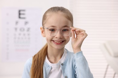 Photo of Little girl wearing glasses near vision test chart at ophthalmologist office