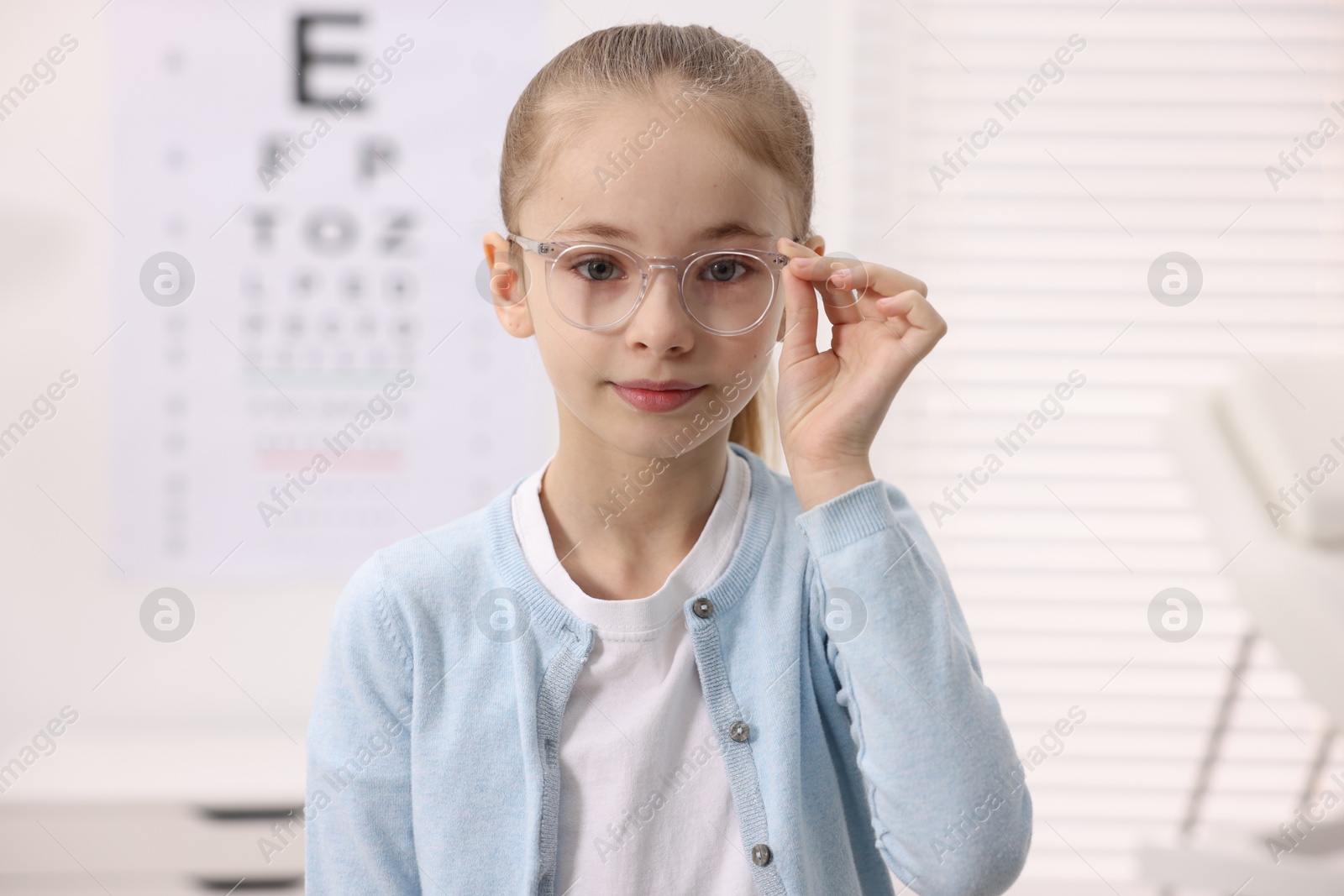 Photo of Little girl wearing glasses near vision test chart at ophthalmologist office