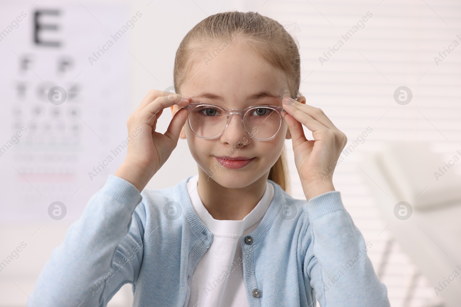 Photo of Little girl wearing glasses near vision test chart at ophthalmologist office