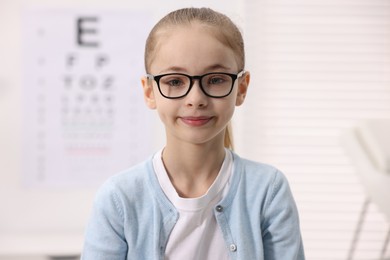 Photo of Little girl wearing glasses near vision test chart at ophthalmologist office