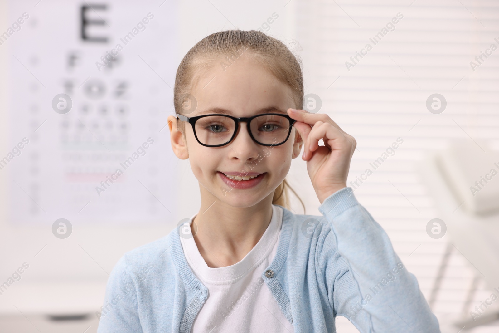 Photo of Little girl wearing glasses near vision test chart at ophthalmologist office