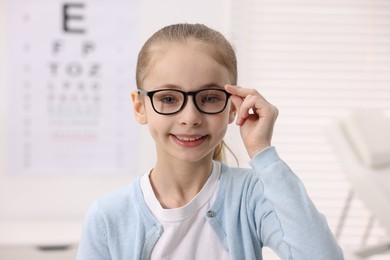 Photo of Little girl wearing glasses near vision test chart at ophthalmologist office