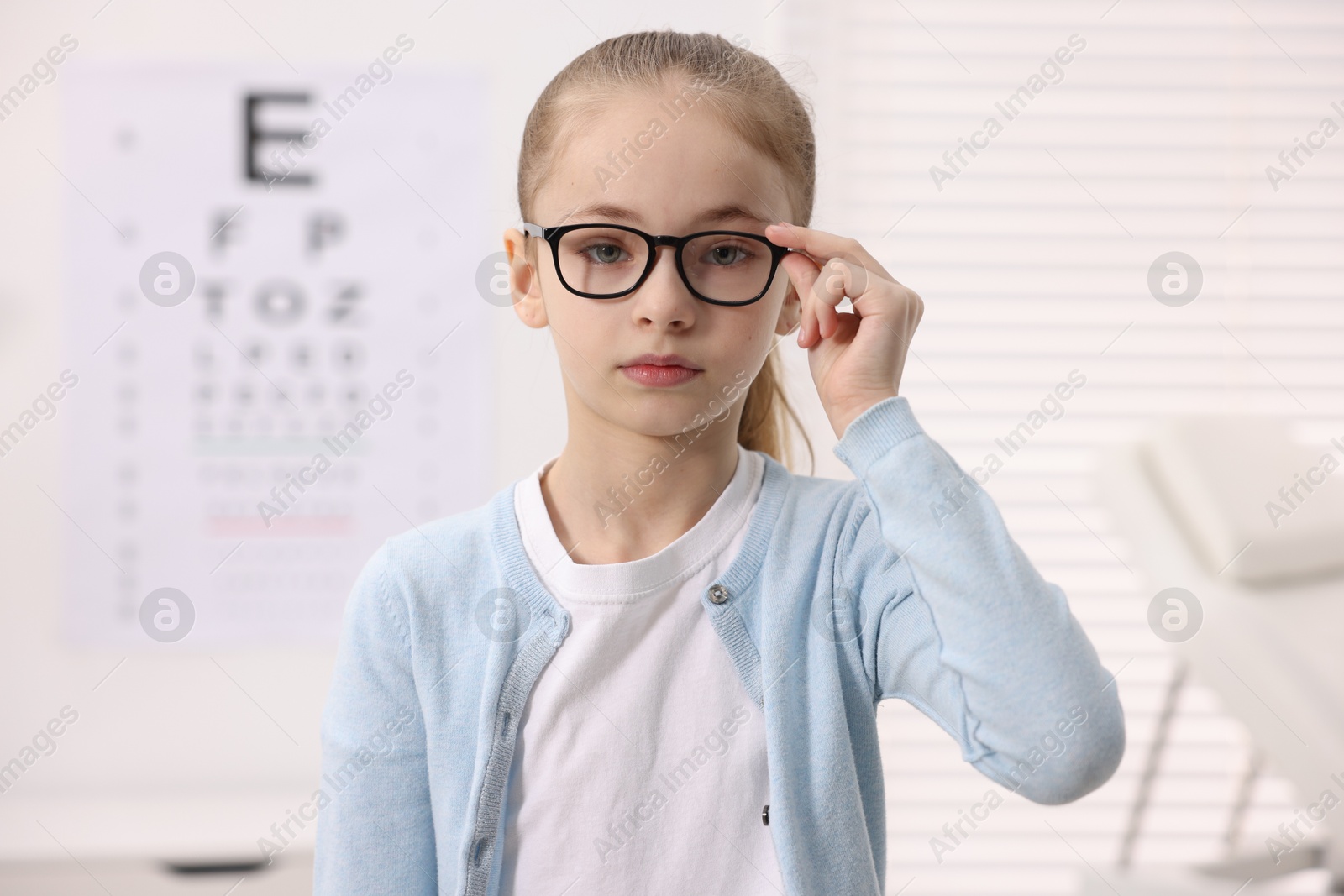 Photo of Little girl wearing glasses near vision test chart at ophthalmologist office