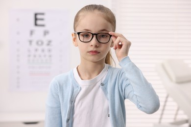 Photo of Little girl wearing glasses near vision test chart at ophthalmologist office